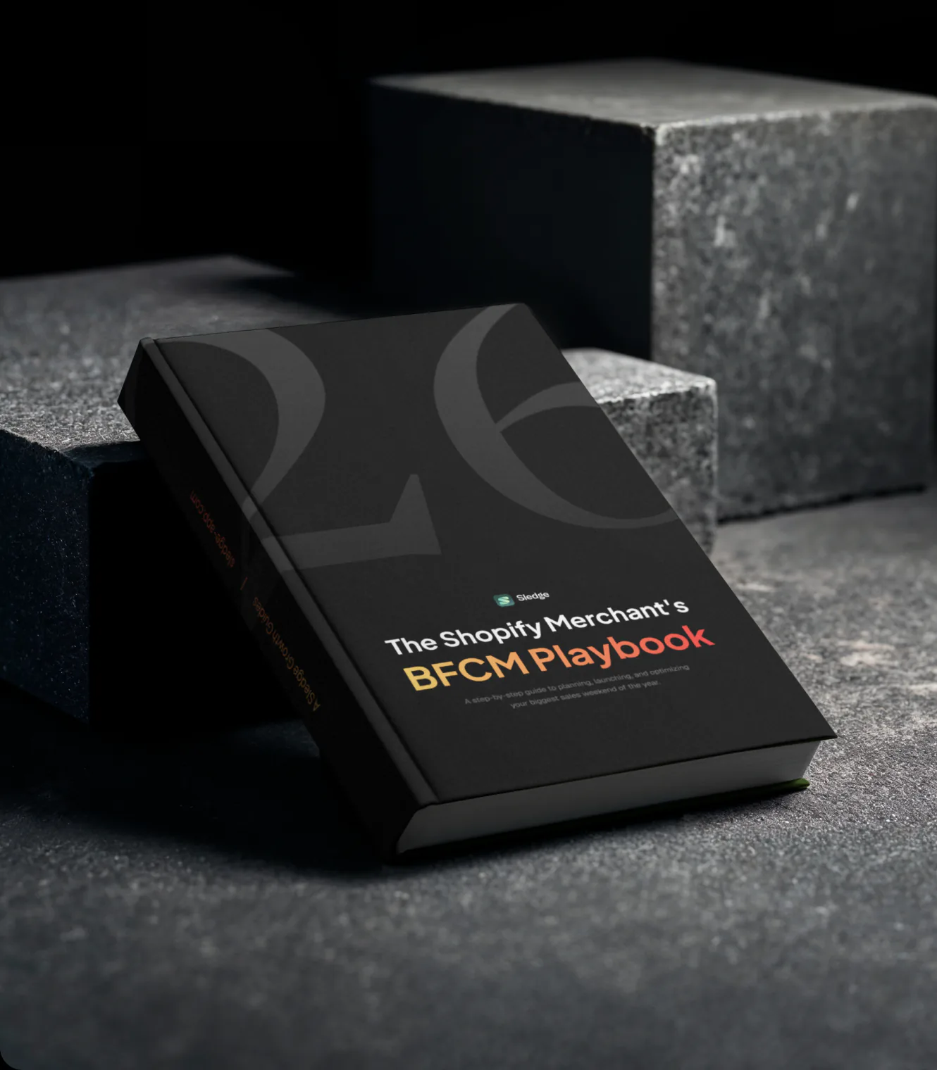 The BFCM Playbook, a black hardcover book with a large 26 on the cover, leaning on dark stone blocks